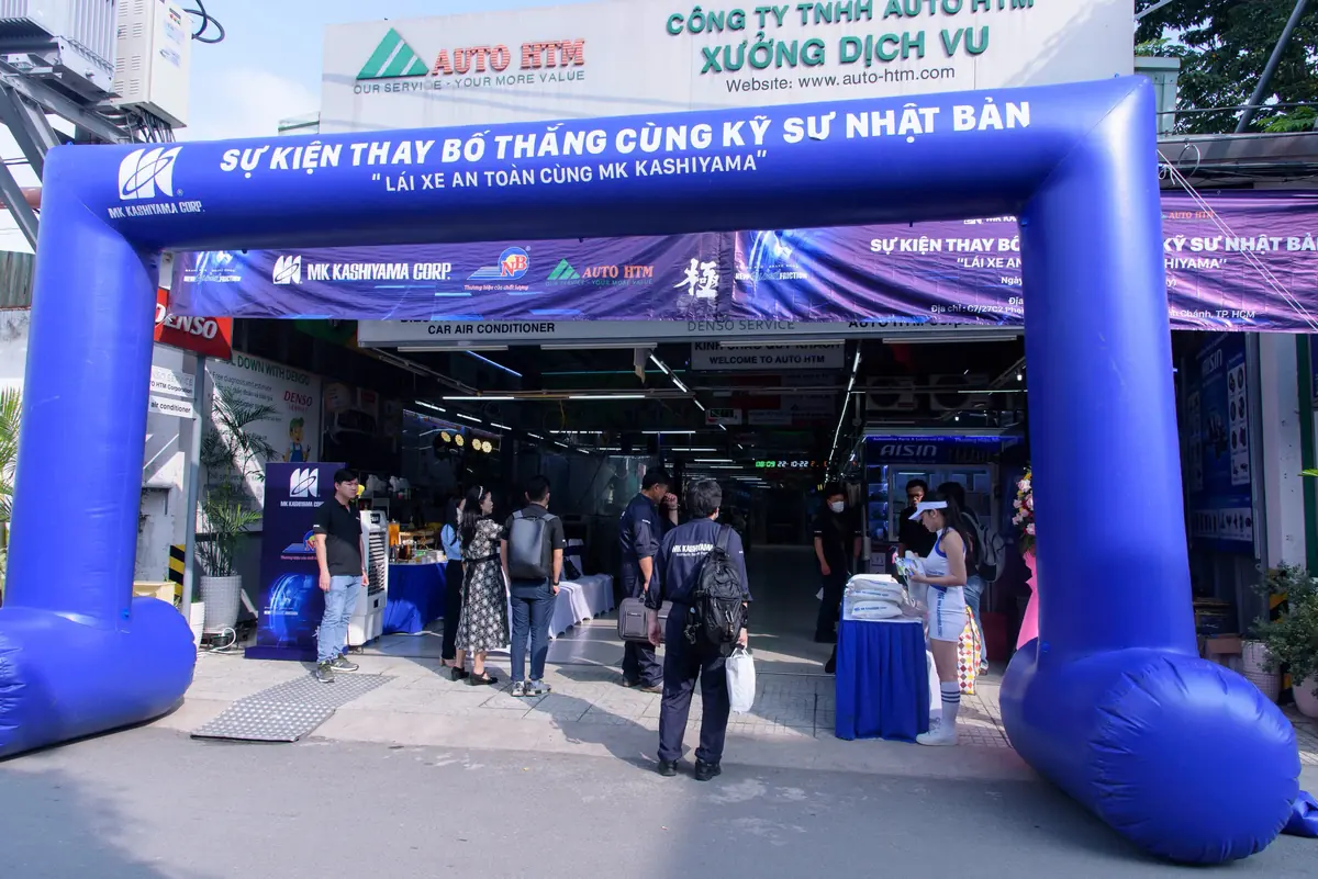 Cổng hơi màu xanh in tên chương trình dựng trước cửa một xưởng dịch vụ ô tô, khách đứng ở lối vào