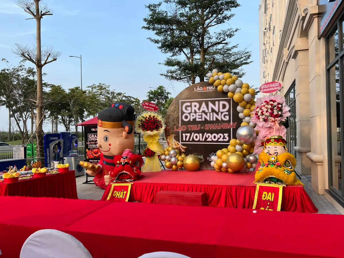 Sân khấu khai trương với backdrop Grand Opening và cổng bong bóng
