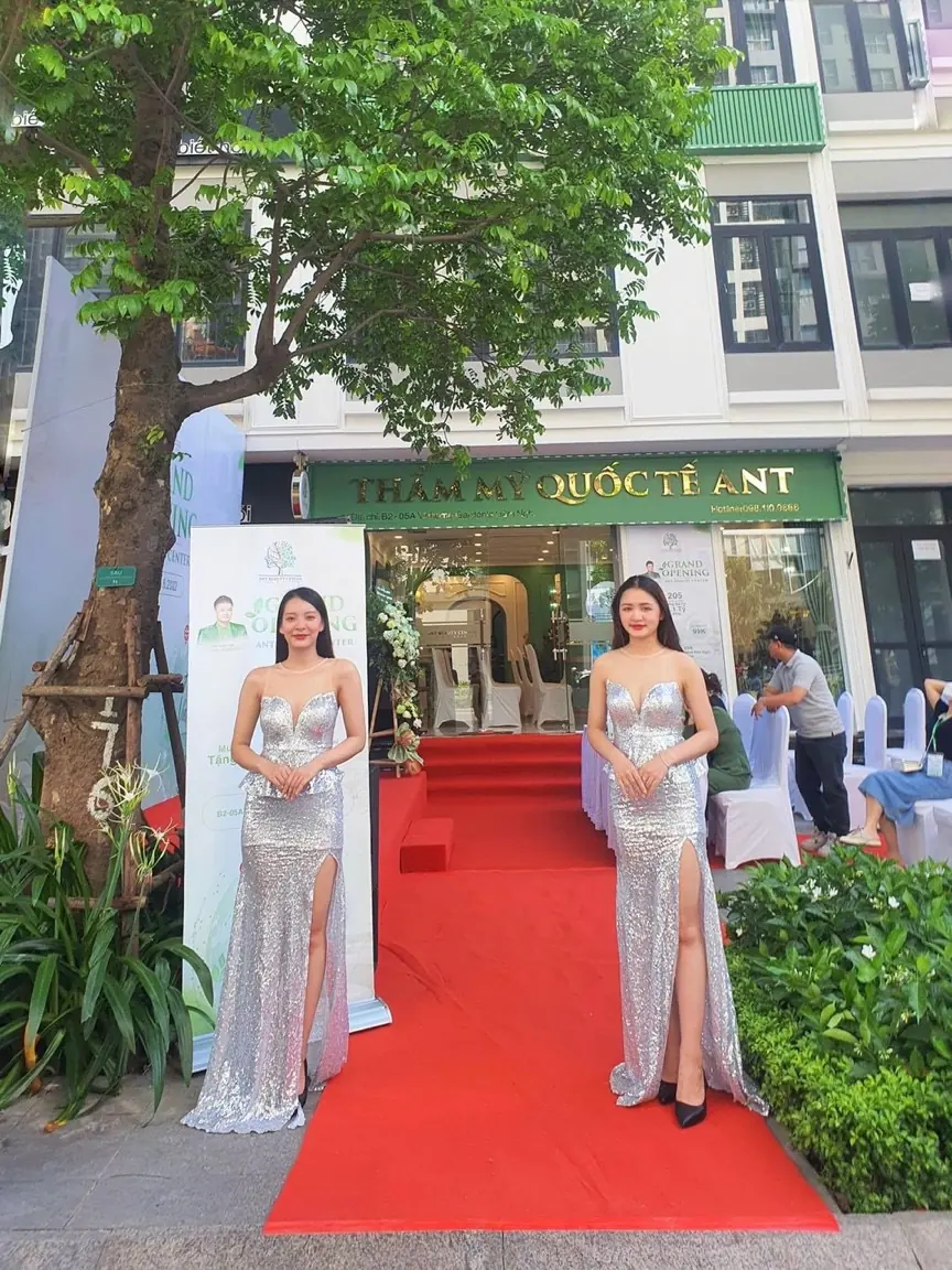 Hai lễ tân đứng hai bên thảm đỏ trước cửa hàng khai trương